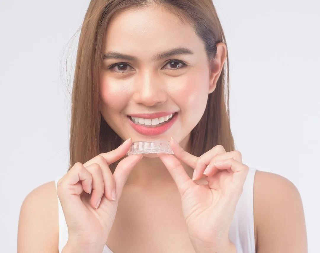 Woman smiling while holding a clear aligner tray